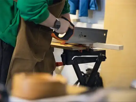 Handcrafted trainee sawing a piece of wood in the workshop